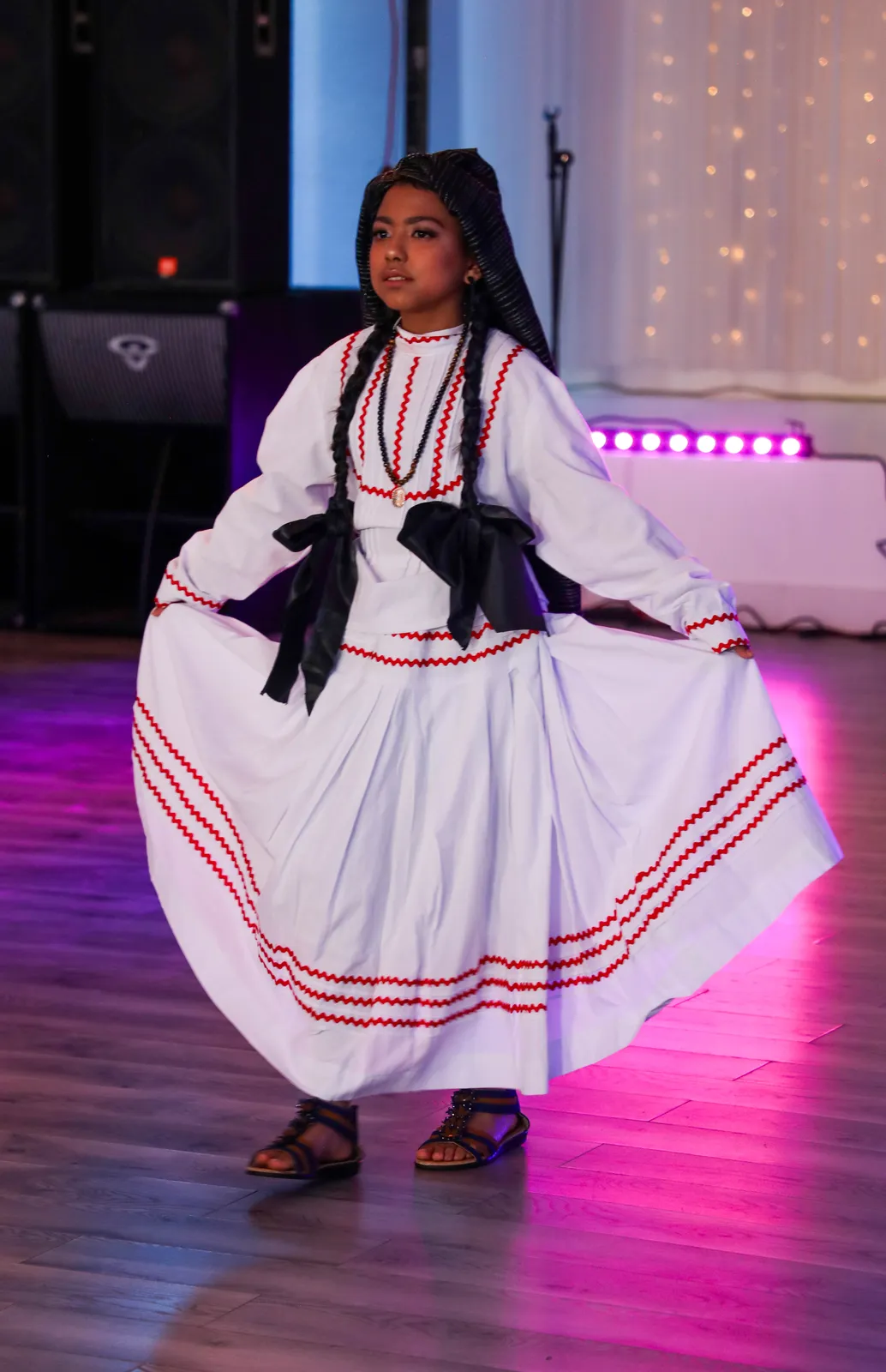 White blouse and skirt with pink ribbon bands and a dark rebozo at Oaxaca en Utah’s Fashion Show 2025