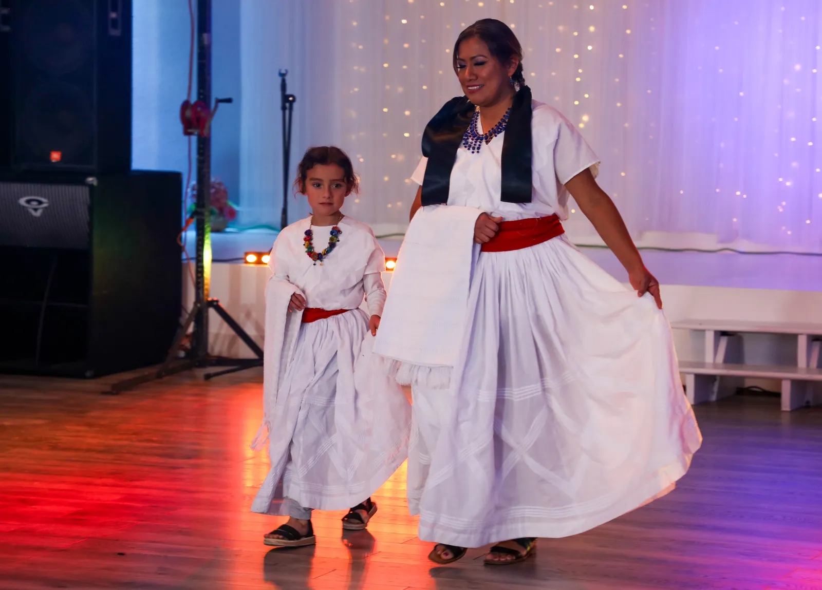Two participants in white huipiles and refajos with woven sashes at Oaxaca en Utah’s Fashion Show 2025