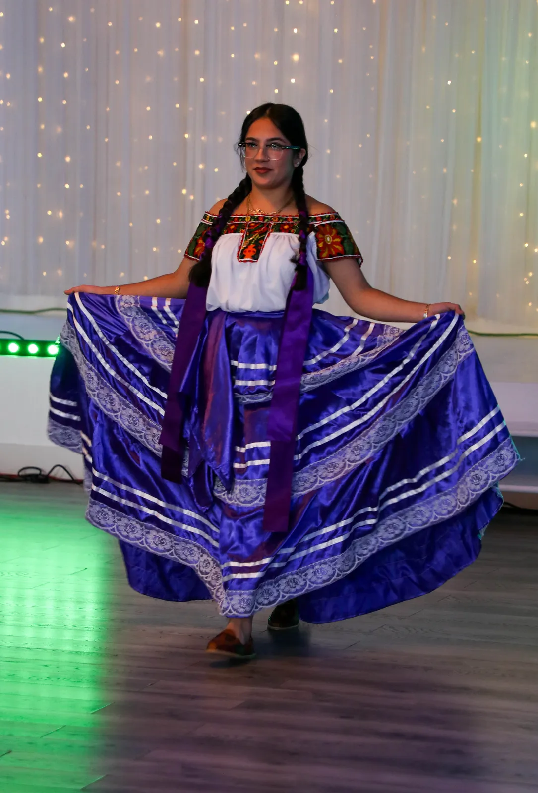 White blouse and purple satin skirt with white lace and ribbon bands at Oaxaca en Utah’s Fashion Show 2025