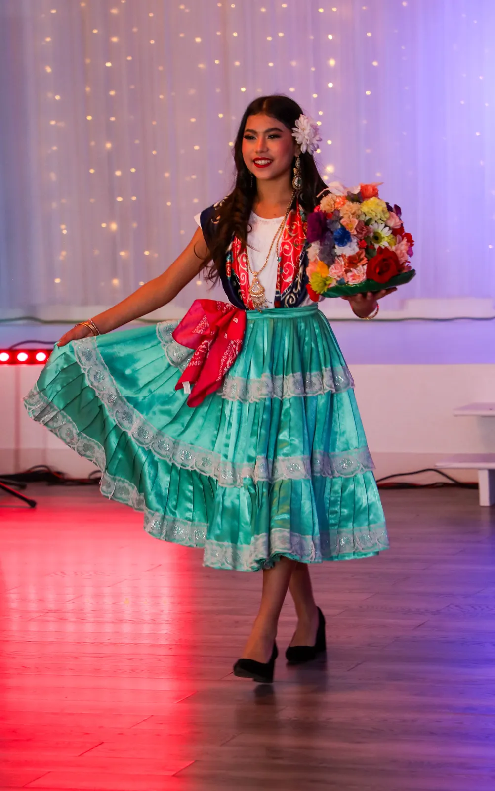 Turquoise satin skirt with lace bands, embroidered blouse, and handkerchief at Oaxaca en Utah’s Fashion Show 2025