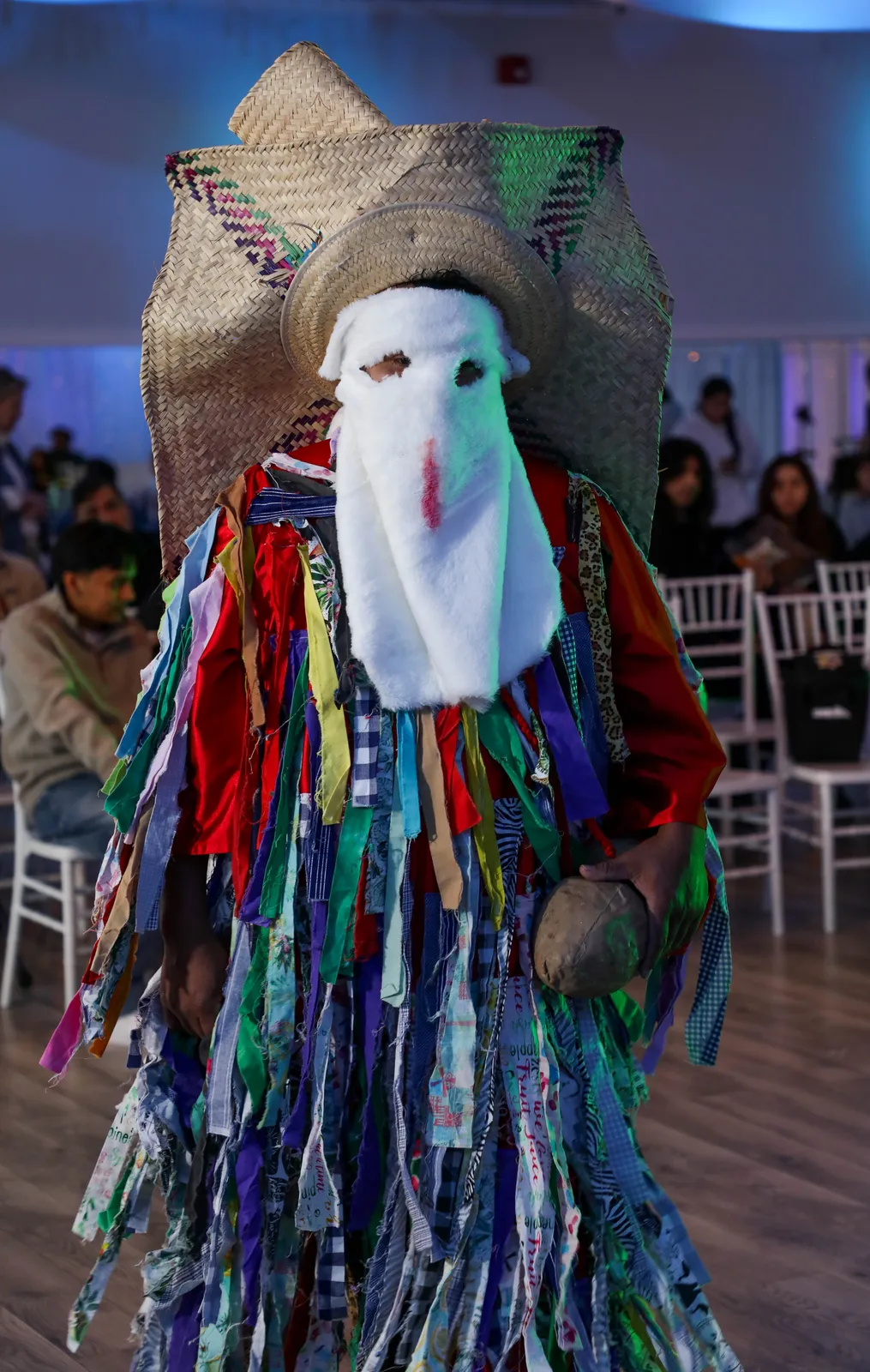 A Tiliche wearing colorful fabric strips, a white mask and a large straw hat at Oaxaca en Utah’s Fashion Show 2025