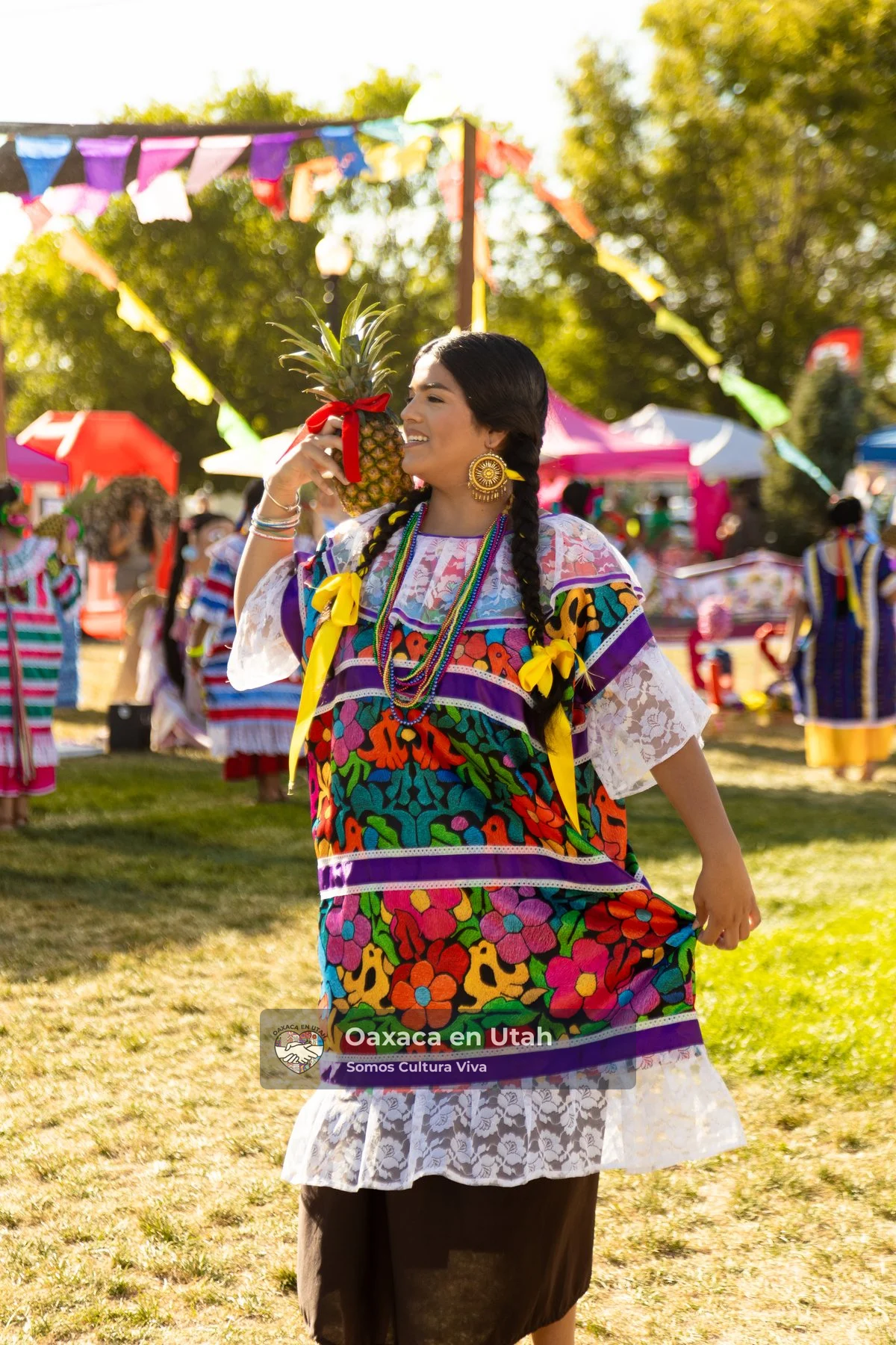 A dancer holds a pineapple while wearing an embroidered huipil