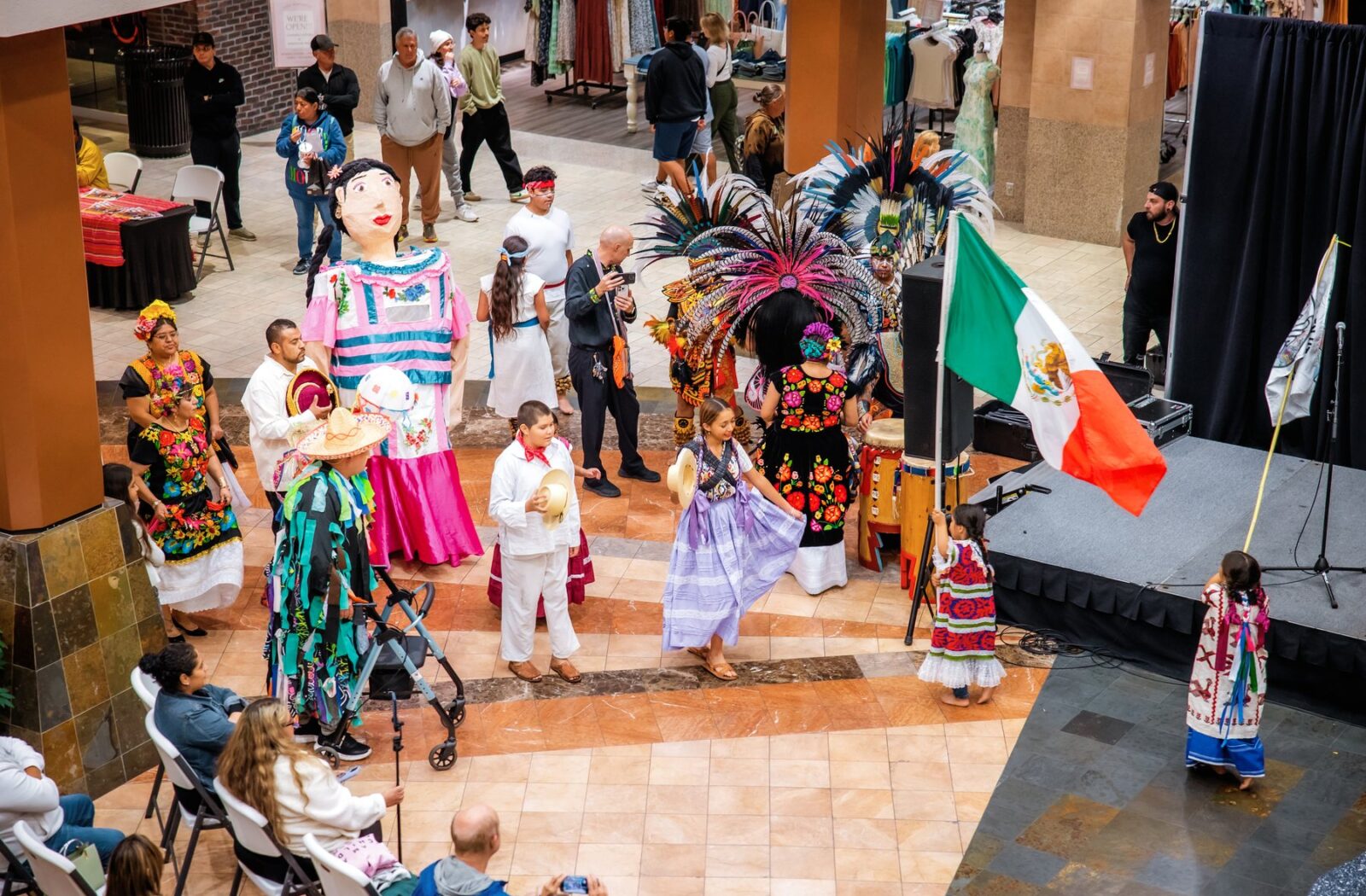 Una vista desde arriba de participantes con una bandera de México reunidos junto al escenario del centro comercial