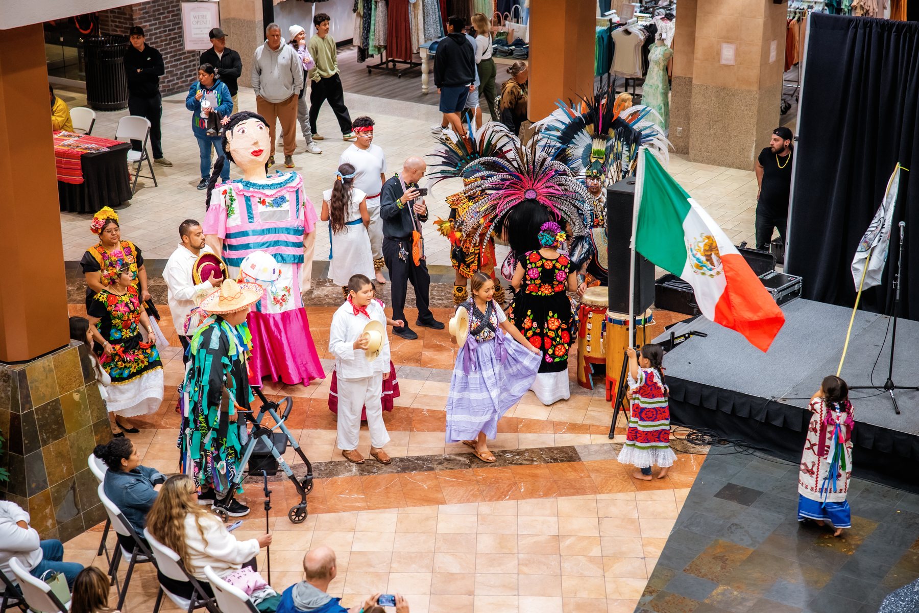 Una vista desde arriba de participantes con una bandera de México reunidos junto al escenario del centro comercial