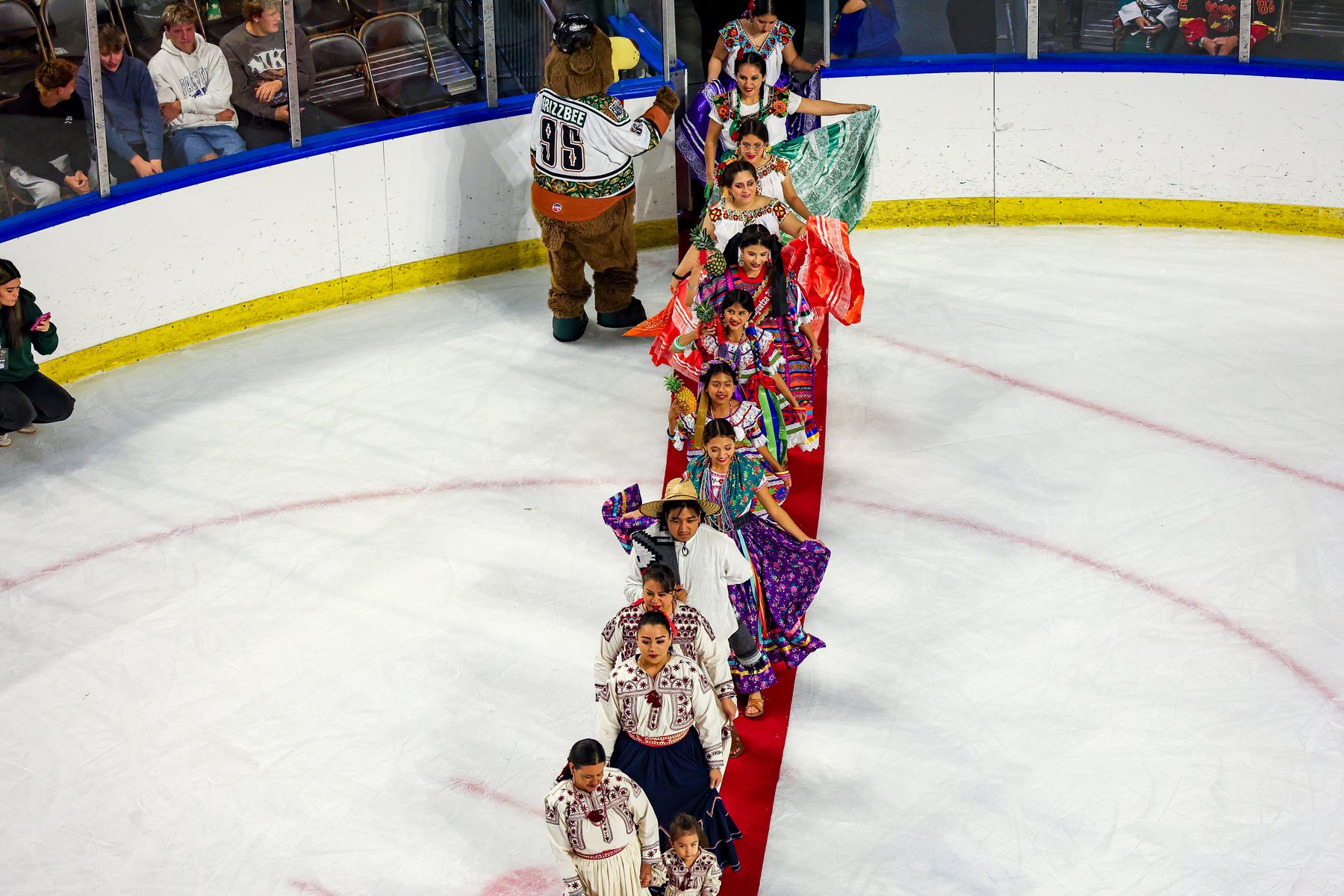 Una fila de participantes con vestimenta colorida cruza el hielo sobre una alfombra roja