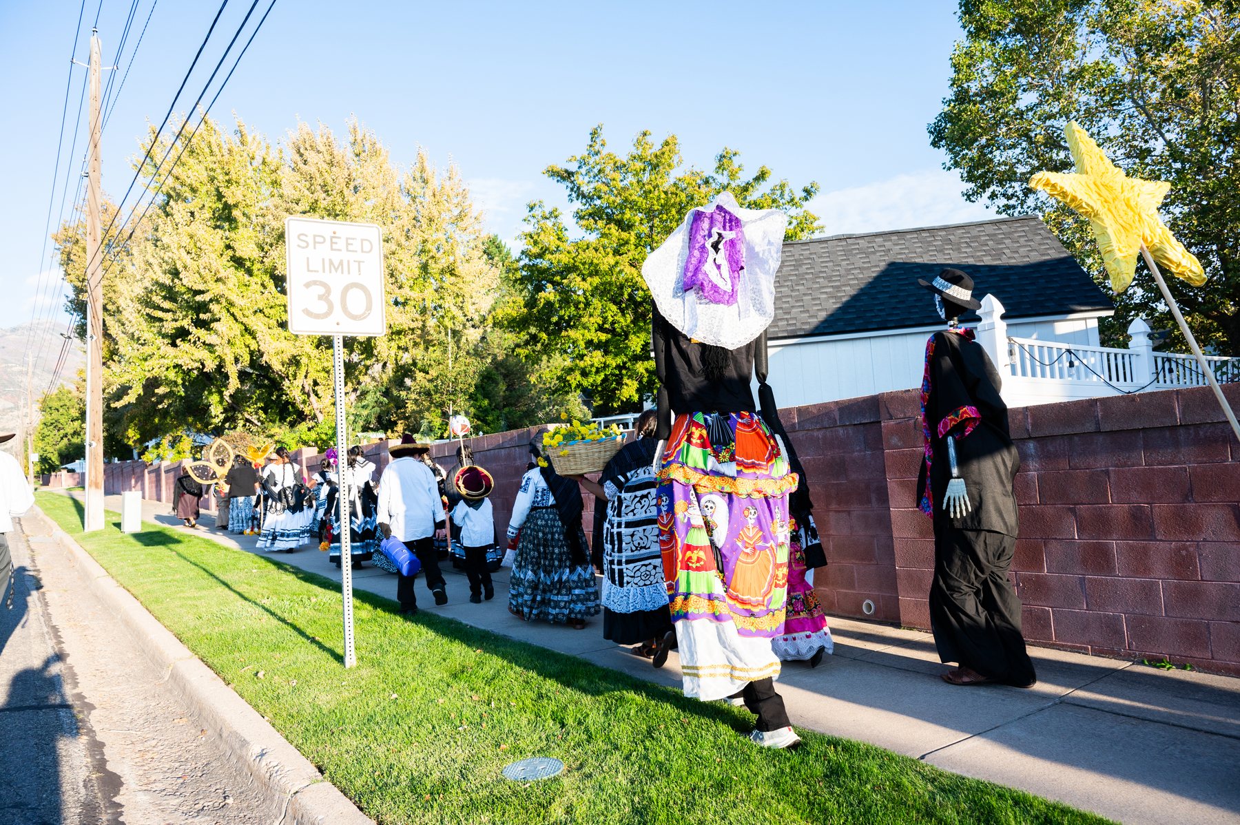 Una procesión por la acera pasa junto al cementerio con una figura alta decorada