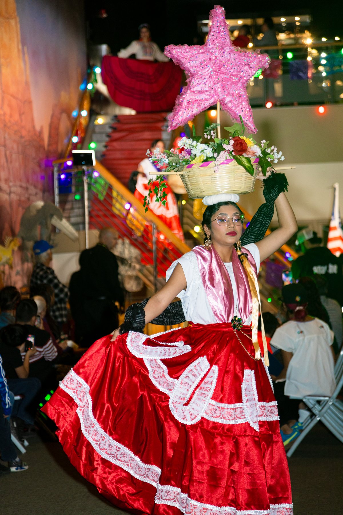 Una participante con vestido rojo y blanco lleva un tocado floral alto coronado por una estrella rosa