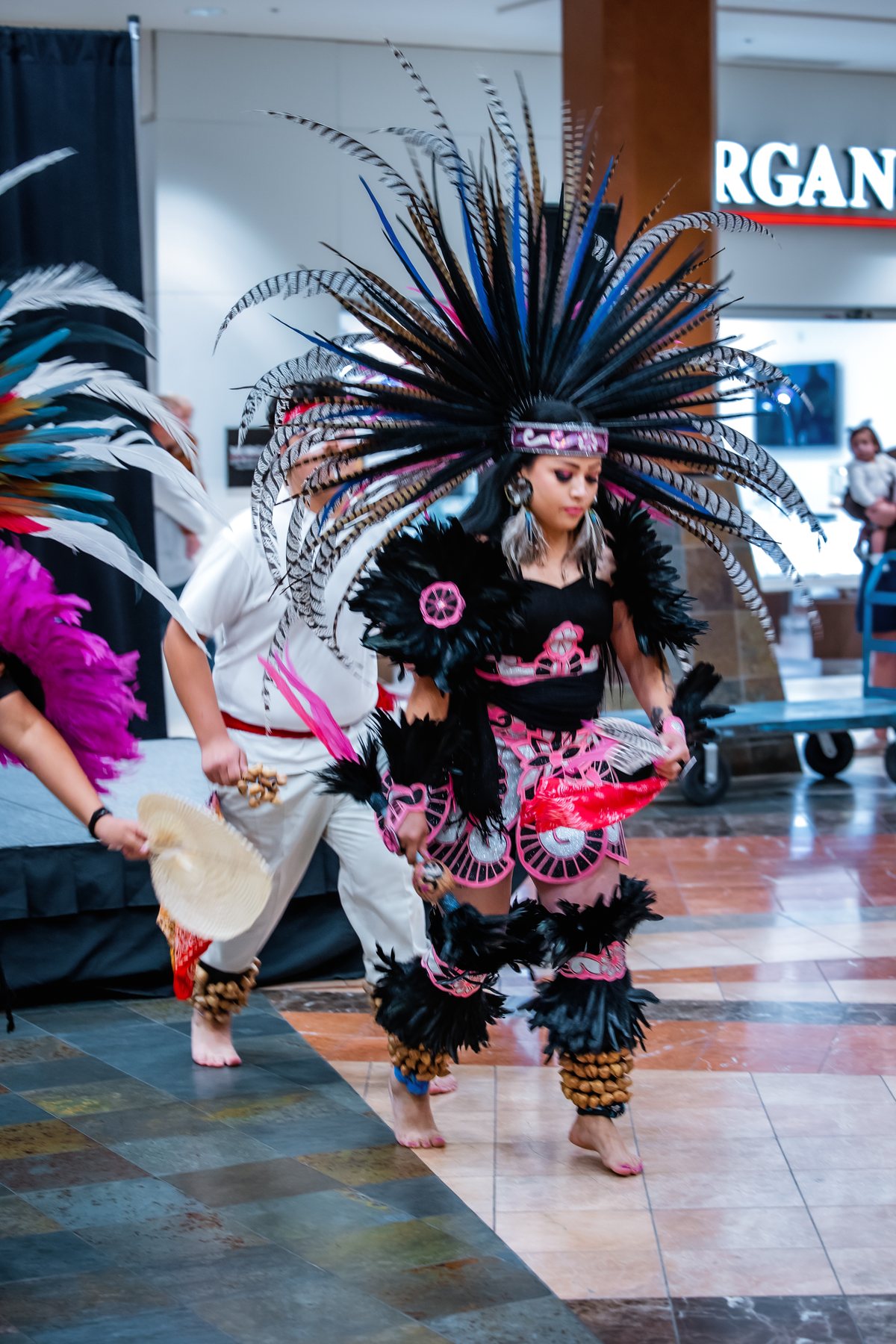 Un artista con un gran tocado de plumas se mueve por el piso del centro comercial