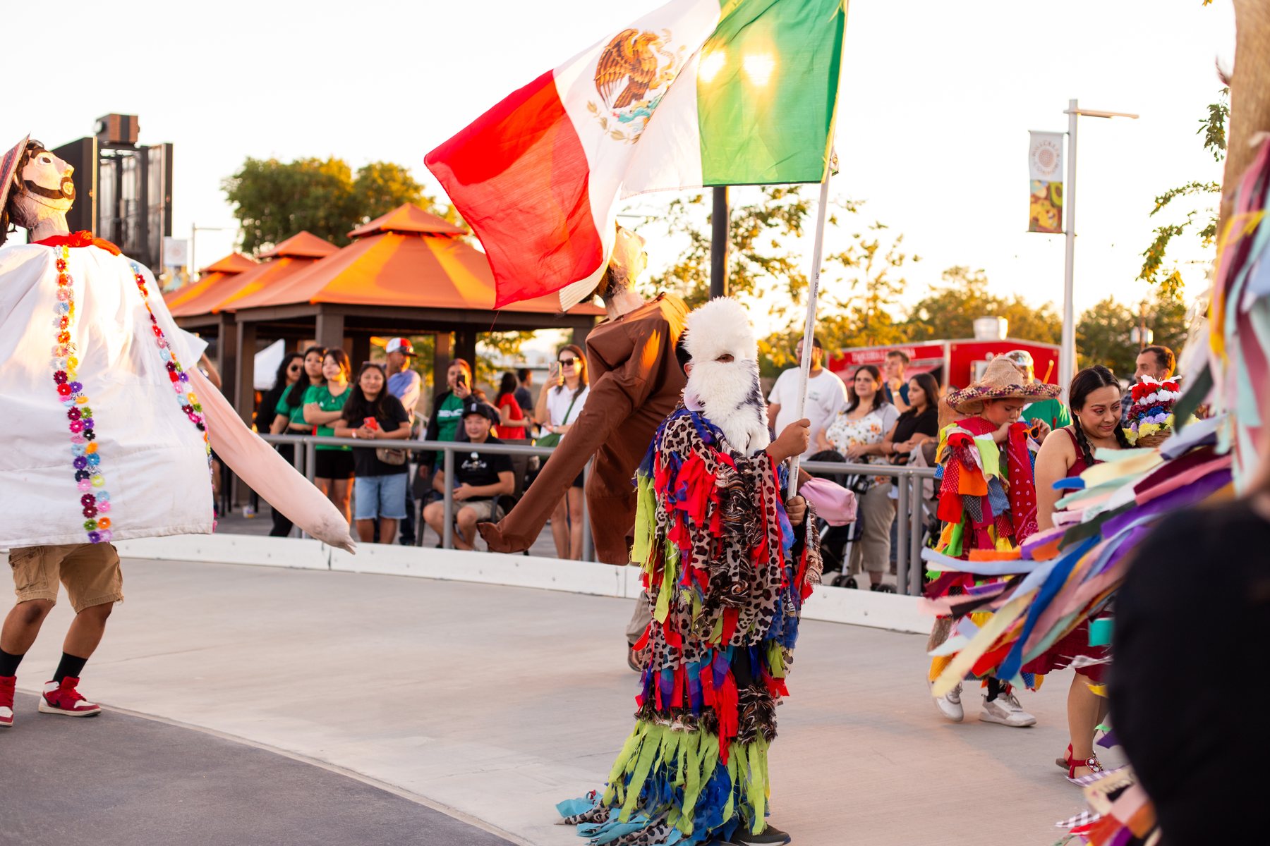 Figuras blancas altas, una bandera de México y un artista cubierto de cintas llenan la plaza