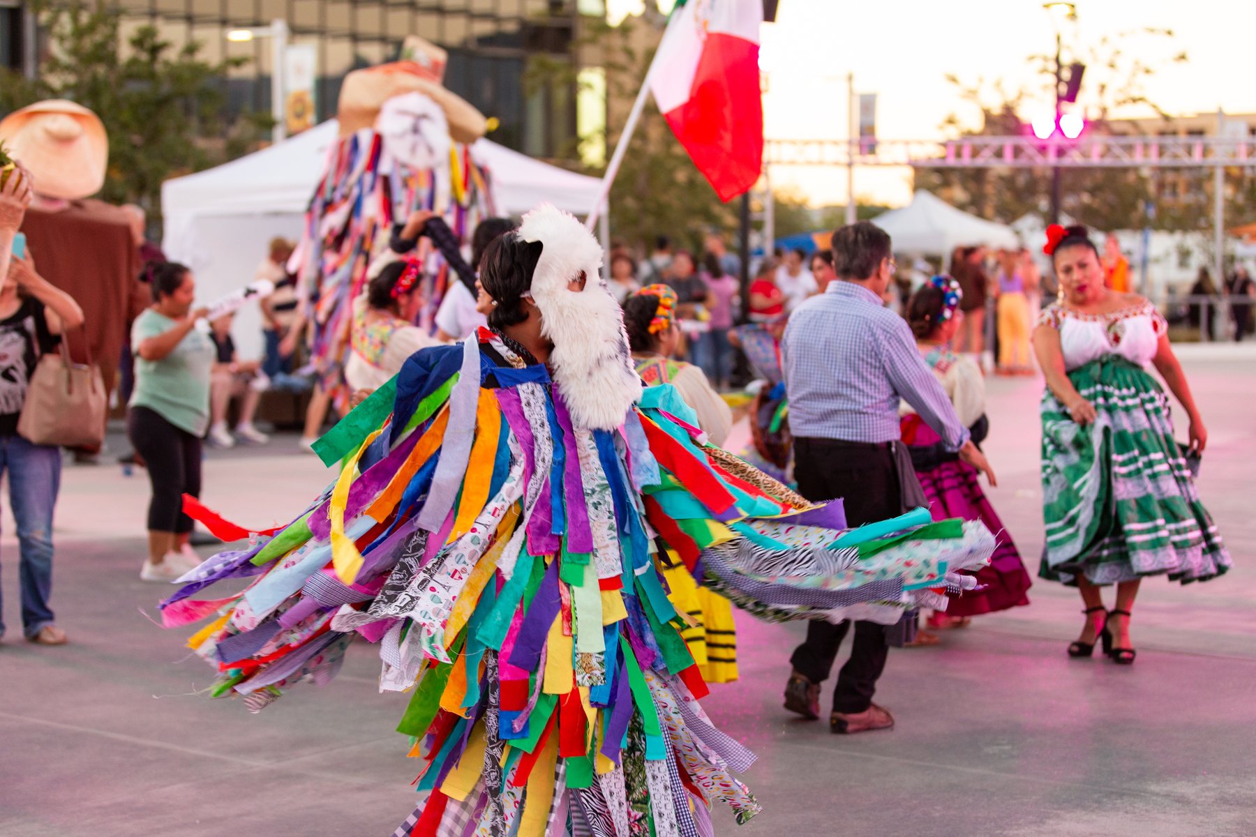 Un artista cubierto de cintas se mueve entre participantes con faldas coloridas