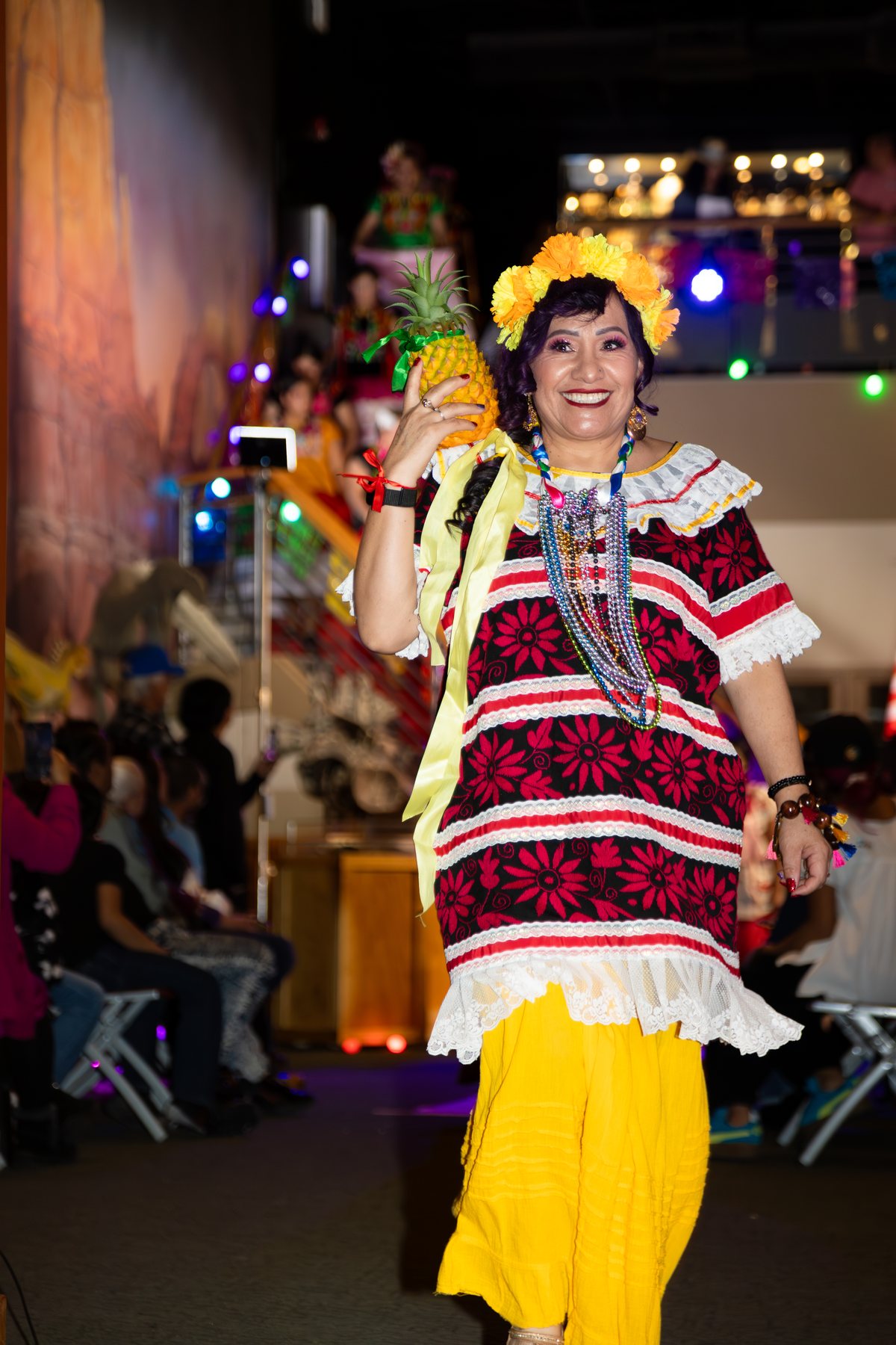 Una participante con blusa tejida negra y roja, falda amarilla y sombrero recorre la pasarela