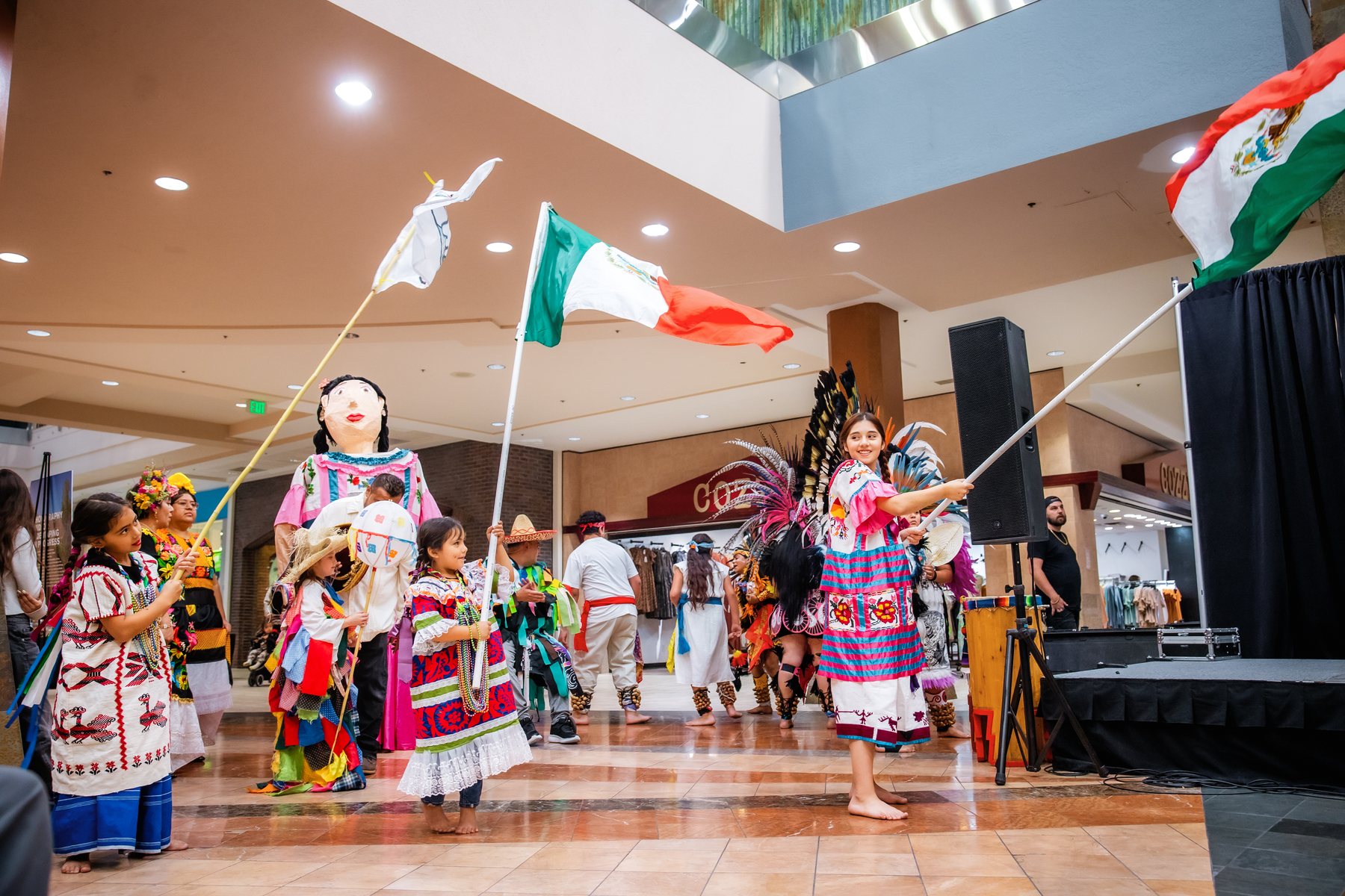 Participantes se reúnen con banderas de México y una figura grande con vestimenta tejida colorida