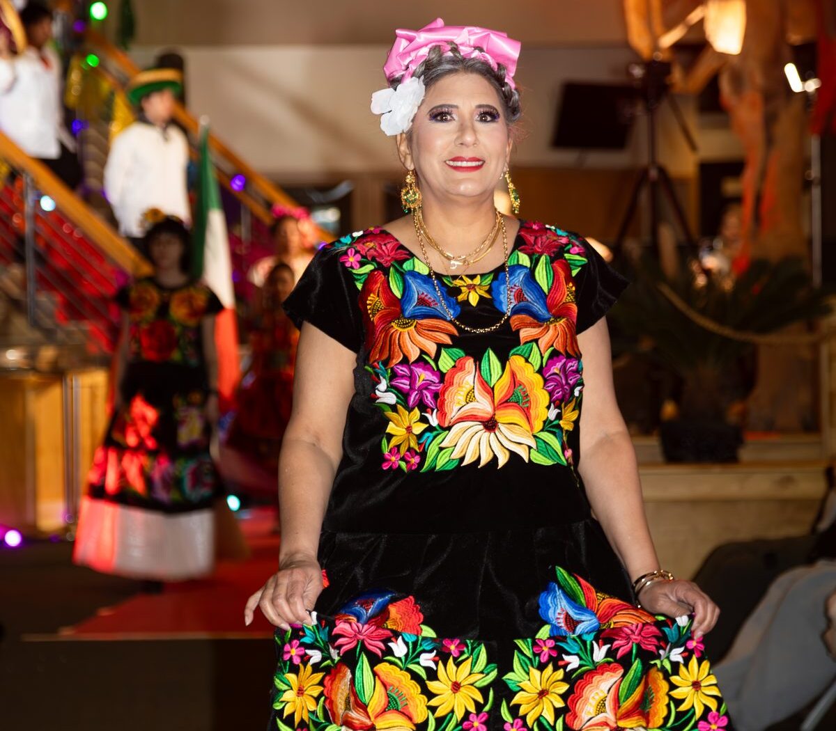 A woman presents a black dress with colorful floral embroidery at the 2026 Oaxaca en Utah Fashion Show