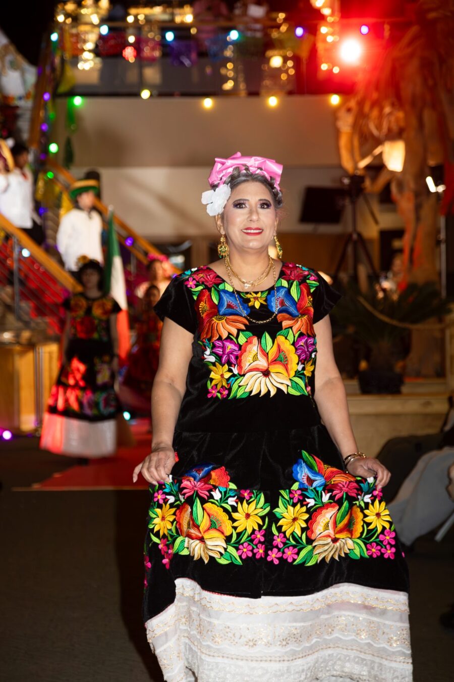 Una modelo presenta un vestido negro con vivos bordados florales multicolor en la pasarela