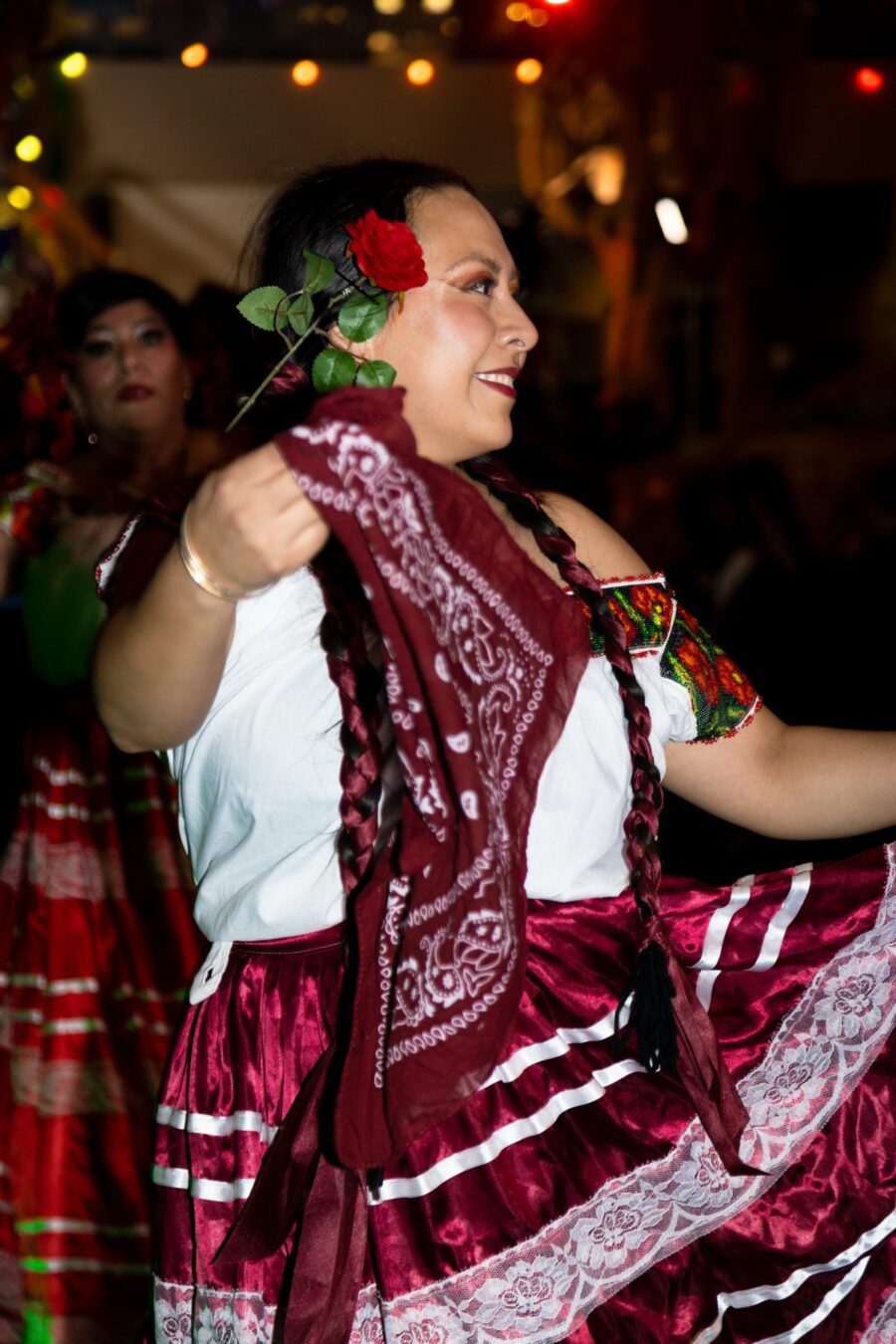 Una bailarina sonríe mientras levanta una falda color vino y un pañuelo a juego durante una presentación