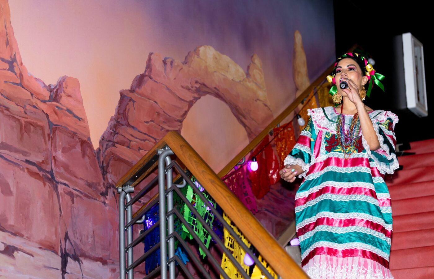 Una artista con vestido verde y rosa canta junto a la escalera con alfombra roja durante el Desfile de Moda 2026 de Oaxaca en Utah