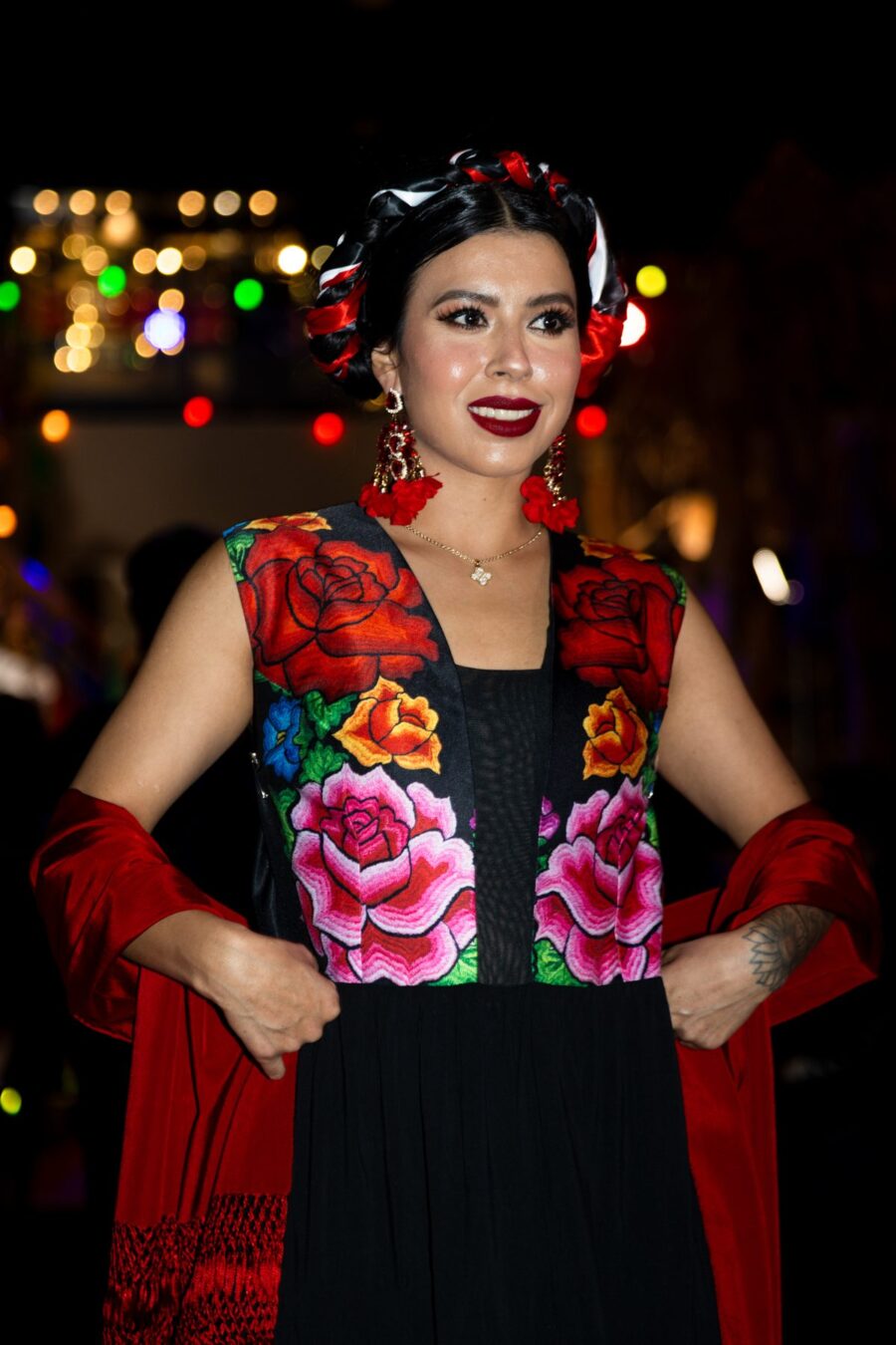 Una modelo vestida de negro con llamativos bordados florales rojos posa bajo las luces de la pasarela