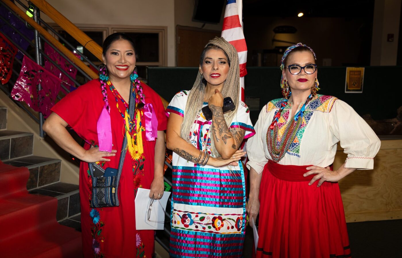 Tres participantes posan con prendas coloridas junto a la escalera decorada