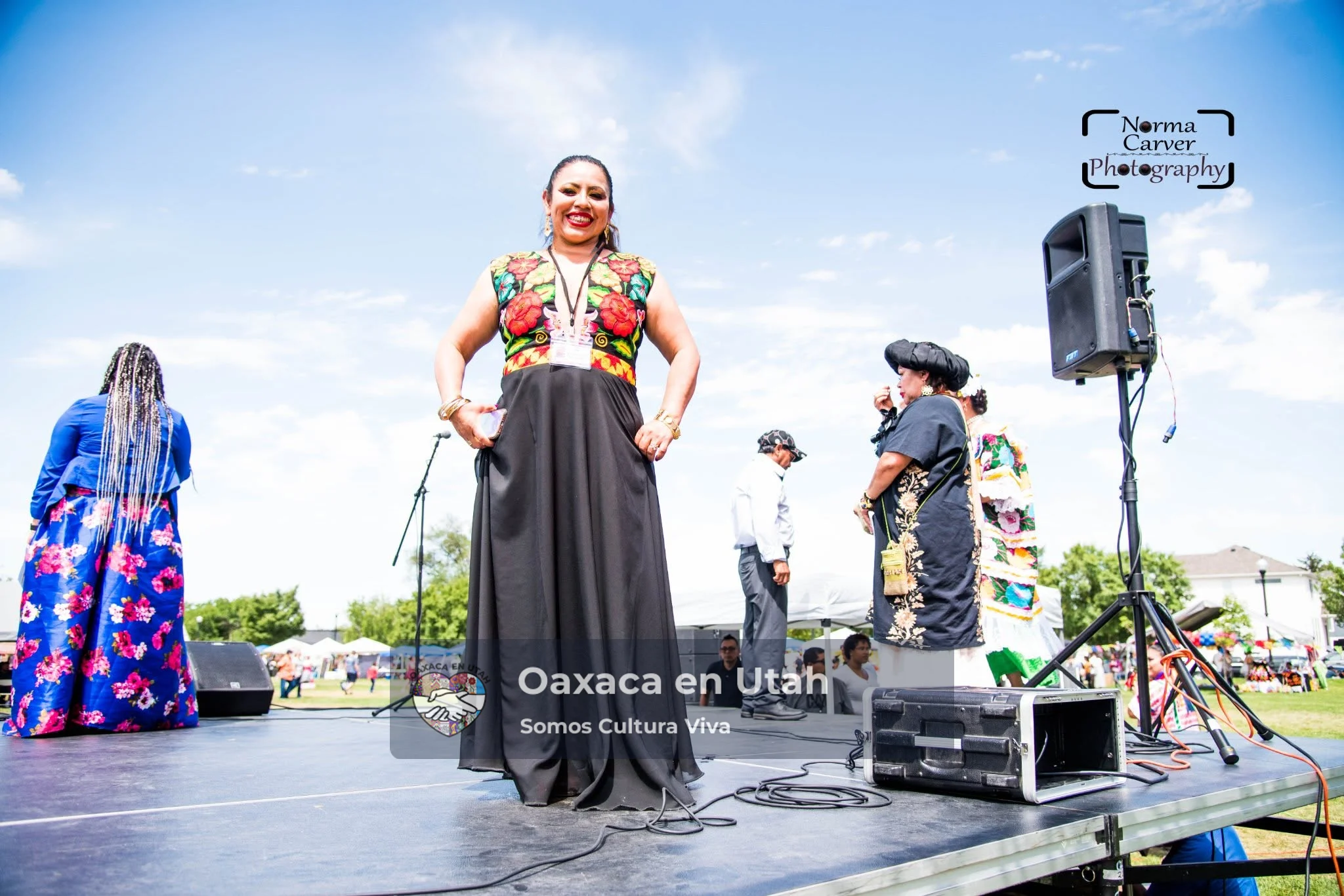 Una organizadora del festival sonríe en el escenario con un vestido negro de bordado floral