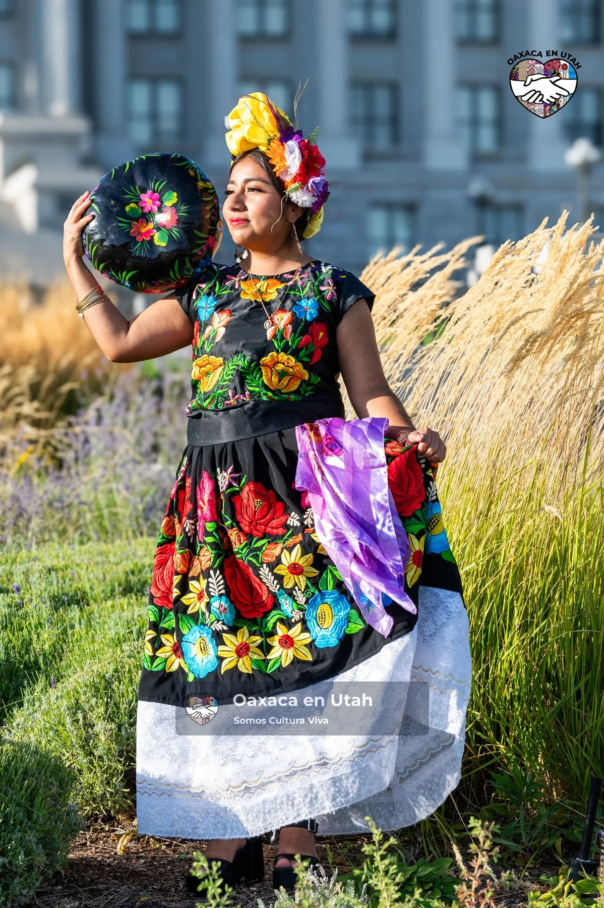 A participant in a black floral top and white skirt holds a basket near the Utah State Capitol