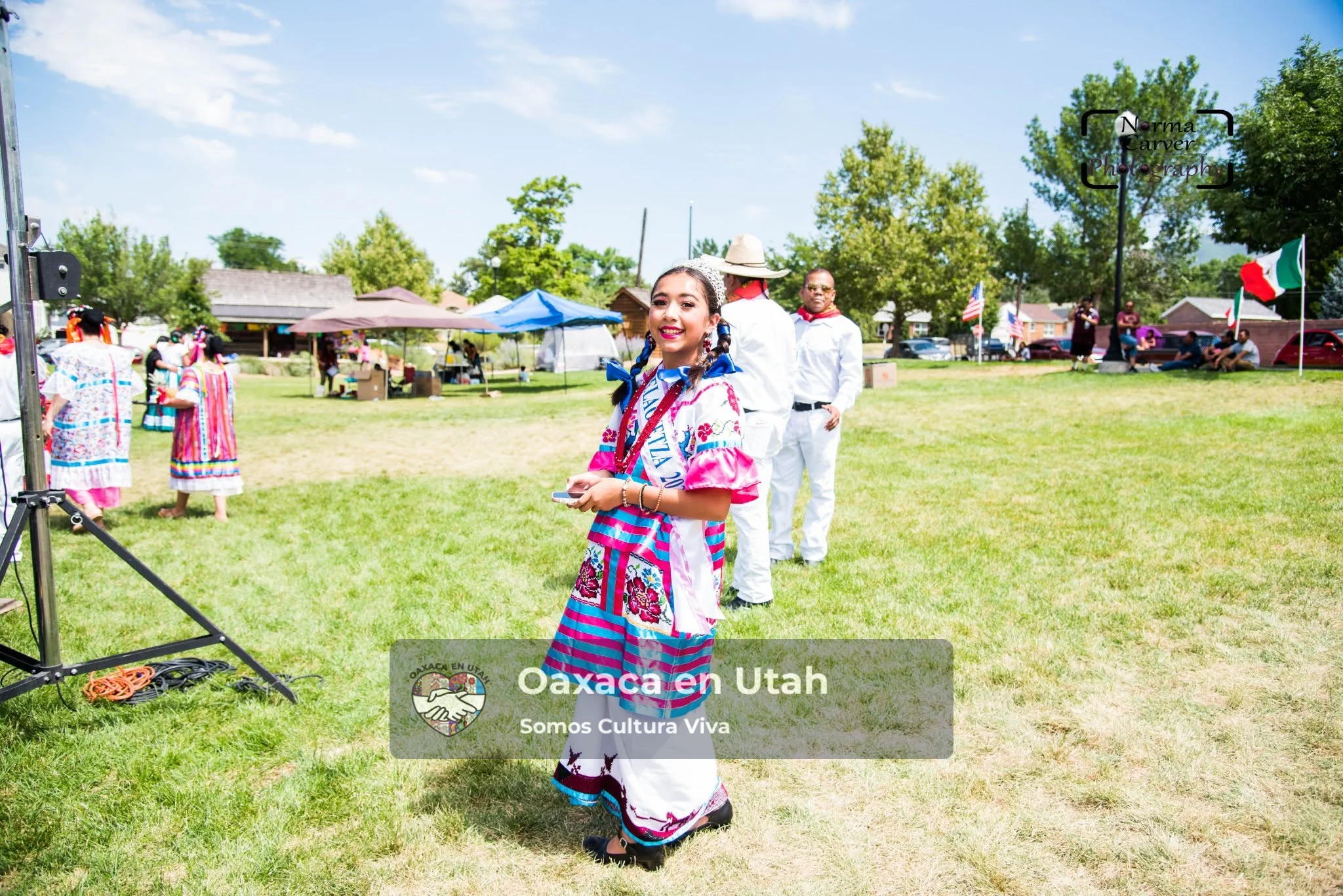 Una joven participante con vestimenta tradicional rosa y turquesa está junto al escenario del festival