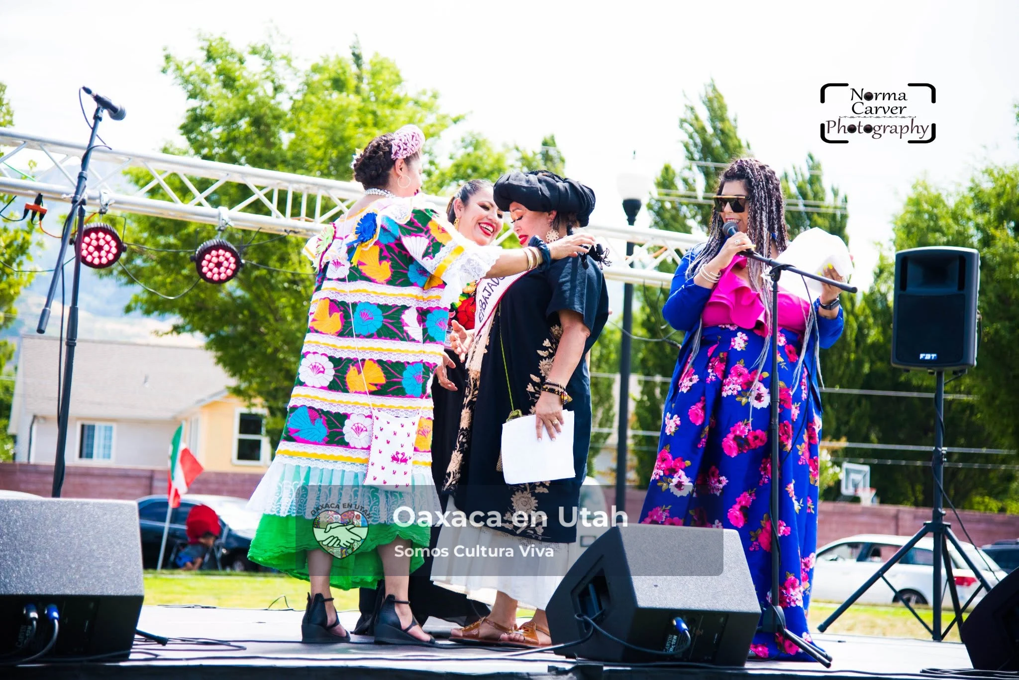 Mujeres con vestimenta tradicional colorida comparten un abrazo durante una presentación en el escenario