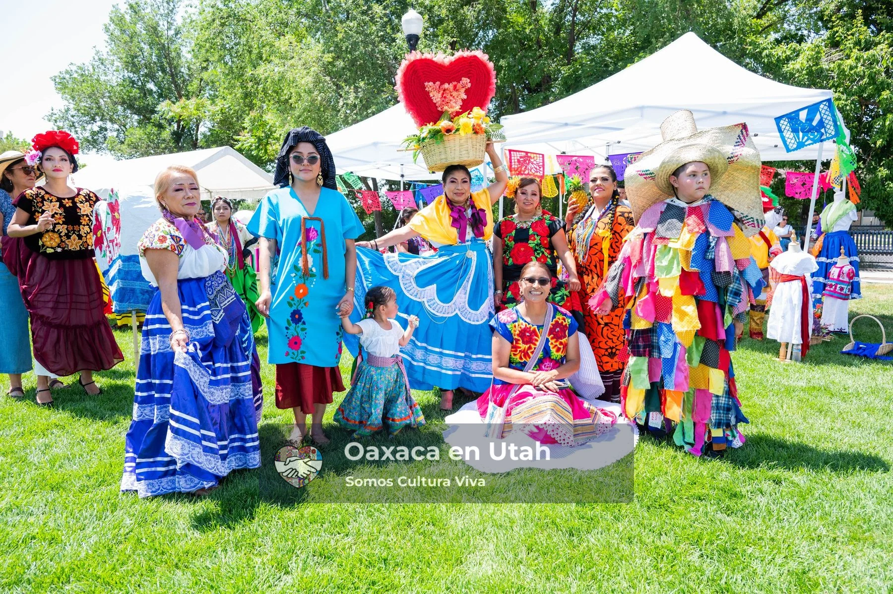 A group in colorful clothing and tall decorated headpieces stands on a festival lawn
