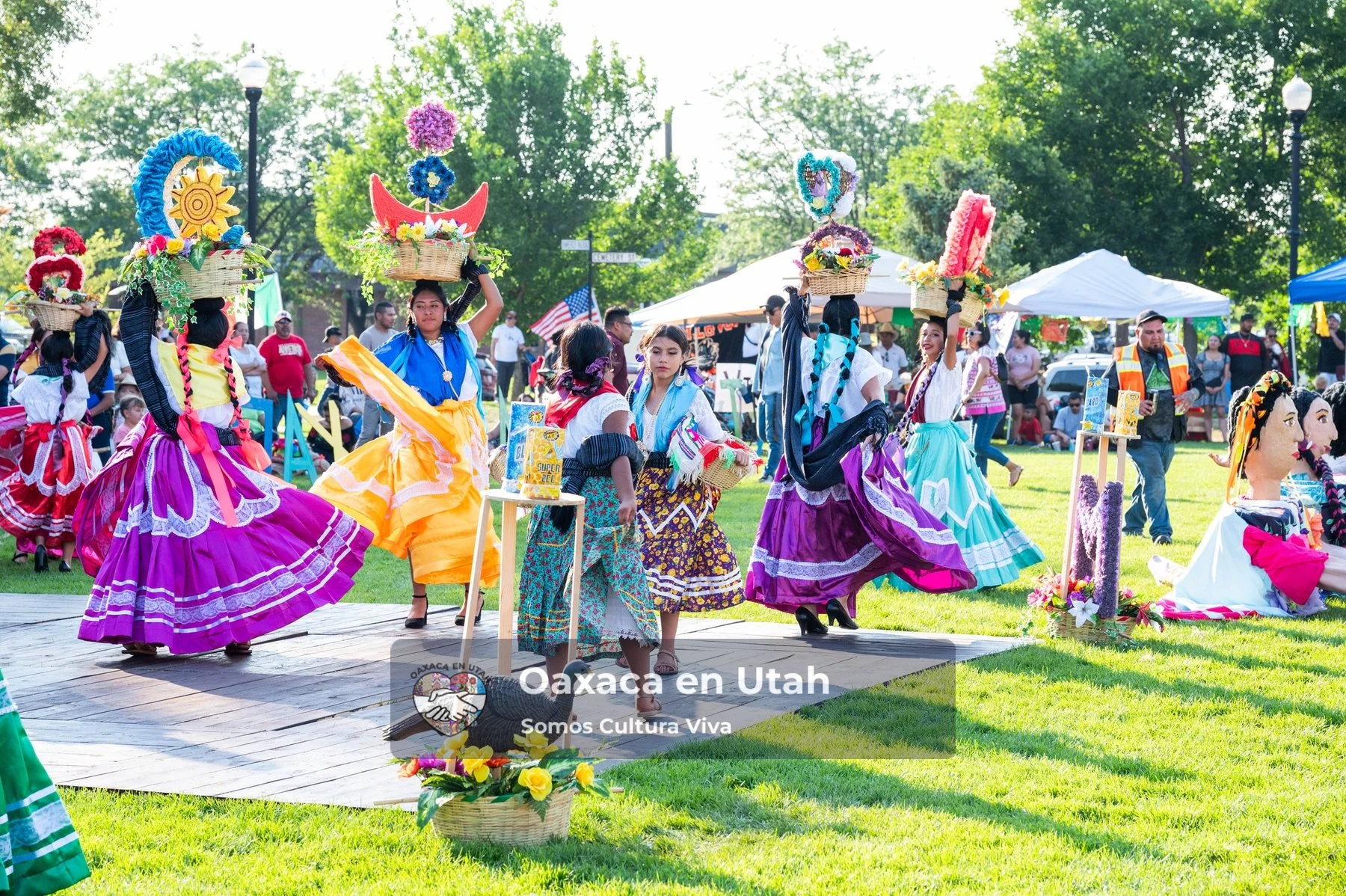 Participants in bright skirts gather around a small decorated structure on the grass