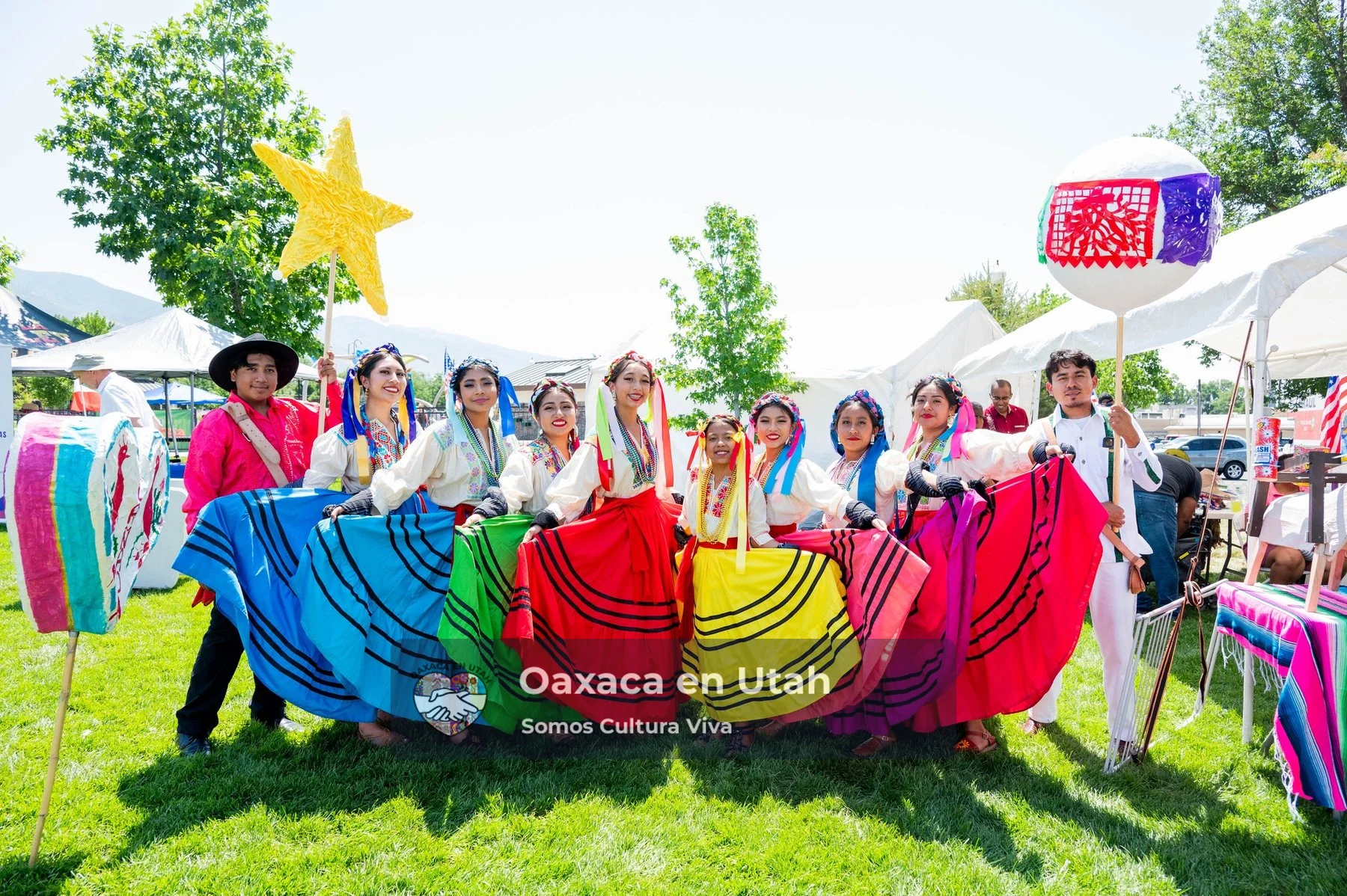 A line of participants displays blue, red, yellow, and green skirts on a festival lawn