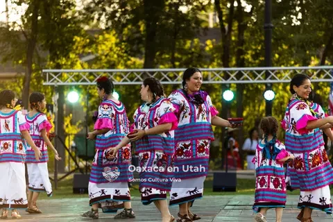 Women and girls in matching magenta woven outfits stand on the stage