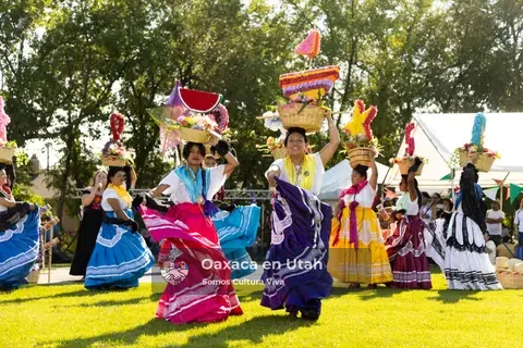 A group in bright skirts moves across the grass wearing tall decorated headpieces