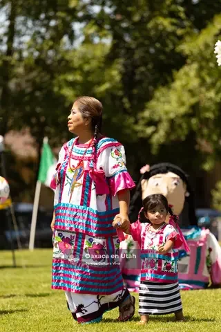 An adult and child in striped embroidered clothing stand near a large festival figure
