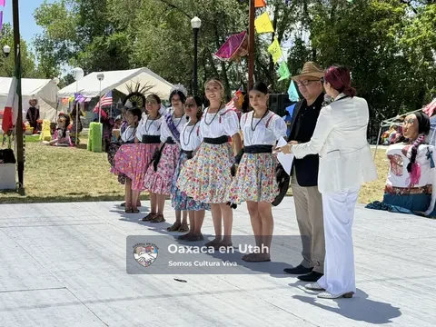 Jóvenes bailarinas con faldas florales junto a presentadores del festival en La Guelaguetza 2026
