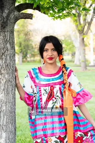 Una participante con vestido de bordado colorido posa junto a un árbol en un parque