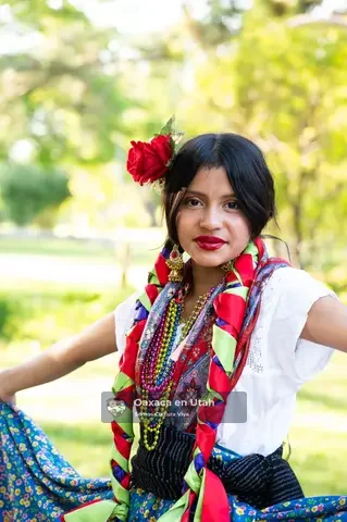 Una participante con trenzas, una flor roja y accesorios tejidos en capas posa en un parque
