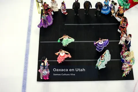 Four participants spread colorful skirts on a black performance area beside the ice