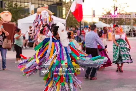 A ribbon-covered performer moves between participants in colorful skirts