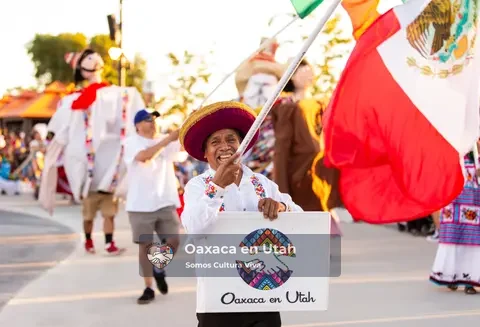 A participant carries a large Mexican flag and an Oaxaca en Utah sign