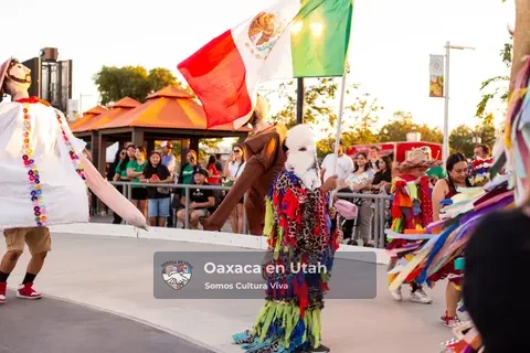 Tall white figures, a Mexican flag, and a ribbon-covered performer fill the plaza